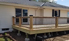 Small elevated wood deck with decorative black railing, built onto a beige siding home in Omaha