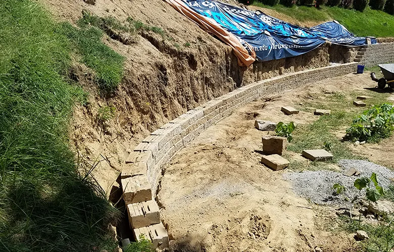 Retaining wall under construction in Omaha with exposed slope and block installation by Liberty Contractors
