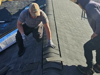 Two contractors performing roofing repair by installing shingles on a residential roof.