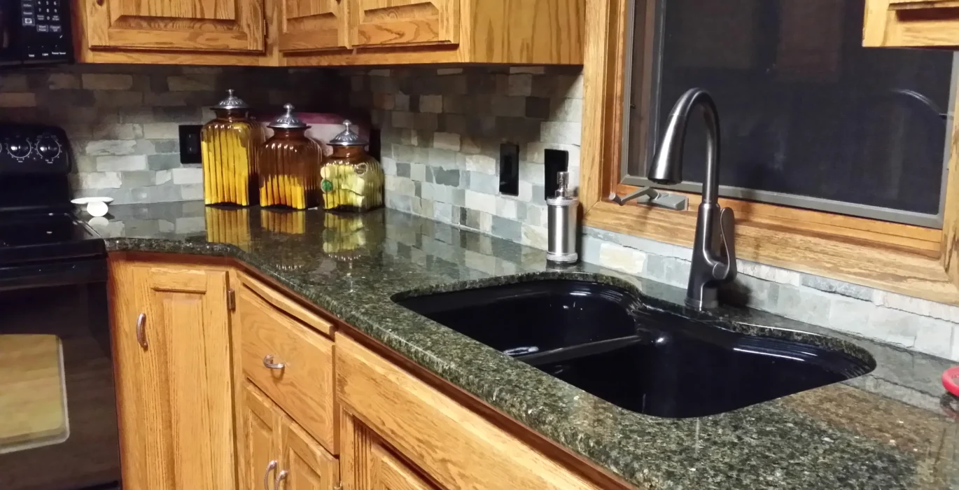 A classic Omaha kitchen with dark granite countertops, oak cabinets, and a black undermount sink featured in a kitchen remodel cost Omaha project.