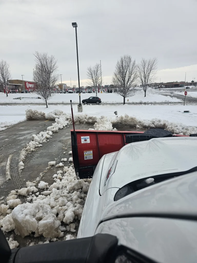 Plow truck pushing snow through retail parking lot during active winter cleanup, keeping drive lanes clear for Omaha businesses.